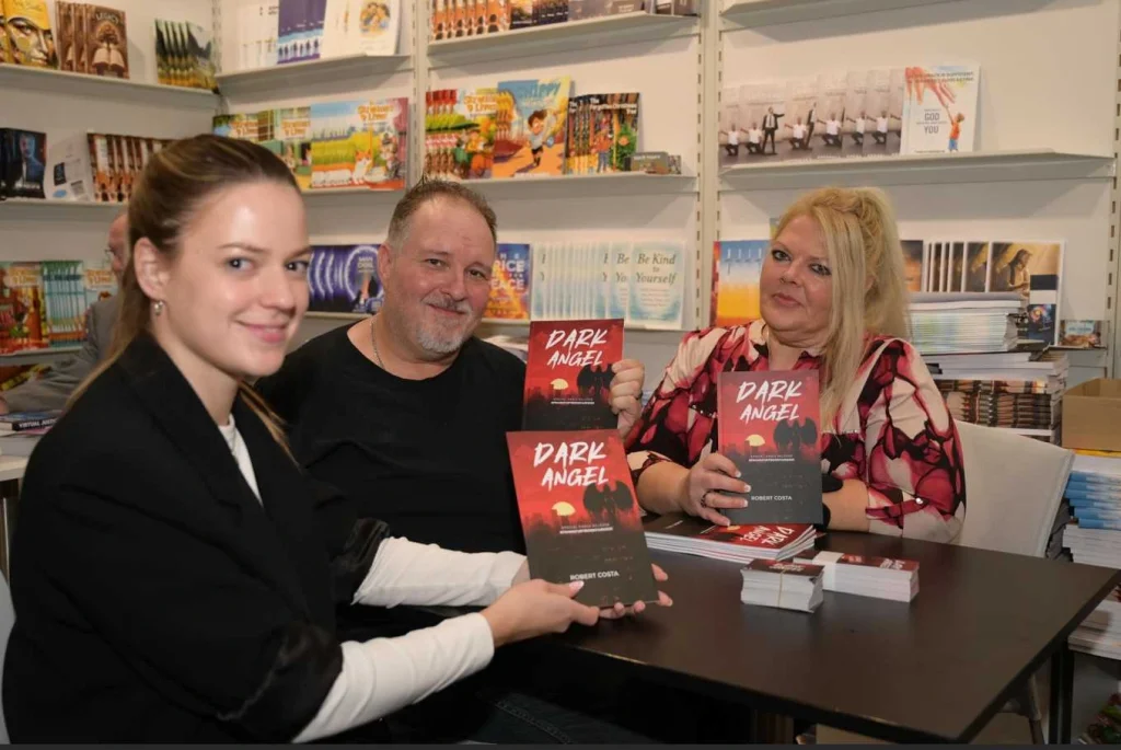 People holding a book titled “Dark Angel” at a signing